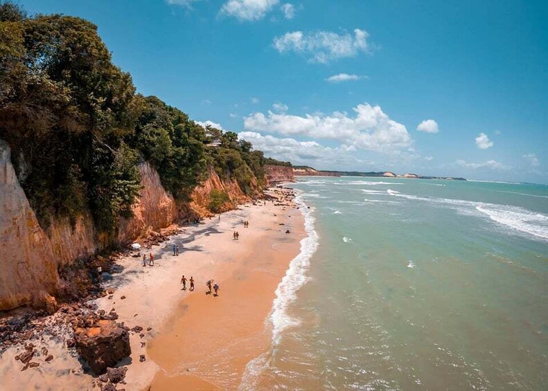 A coastal beach with clear waters, rocky cliffs, and sparse beachgoers. 3
