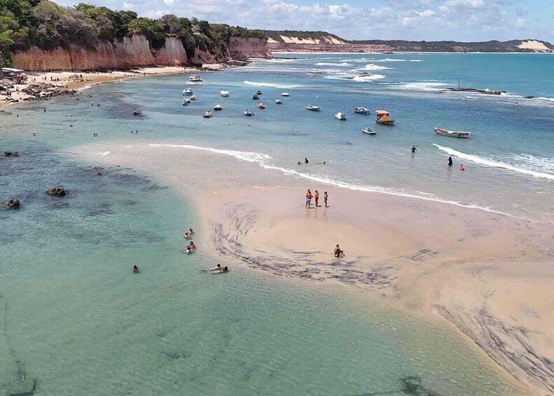 A coastal beach with clear waters, boats, and people swimming and walking on the shore. 2