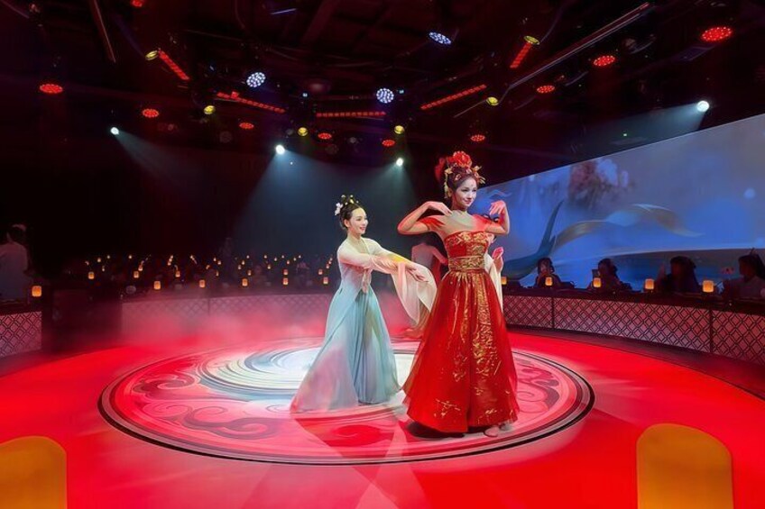 A stage with two performers in traditional costumes, a red carpet, and a large screen in the background. 4