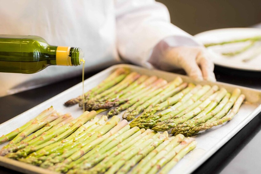 A chef pouring oil over asparagus on a tray. 3