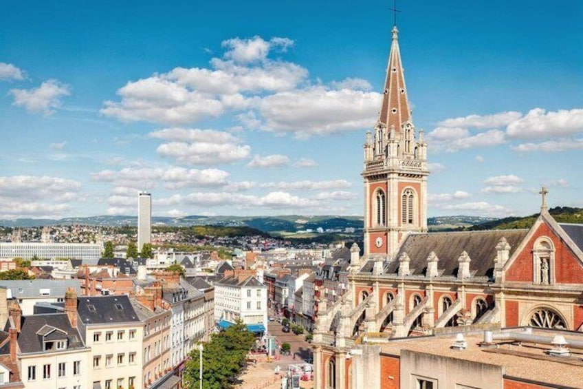 A cityscape with a prominent church tower, a modern building, and a distant mountain range. 1