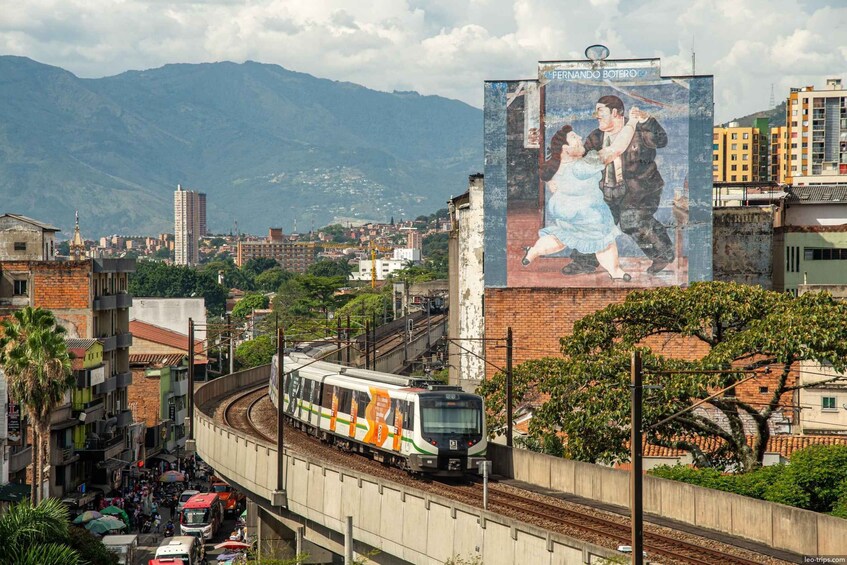 A train on elevated tracks, a mural of a couple, and a mountainous backdrop. 3