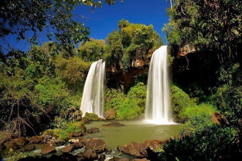 A waterfall with two streams cascading into a pool surrounded by lush greenery. 2
