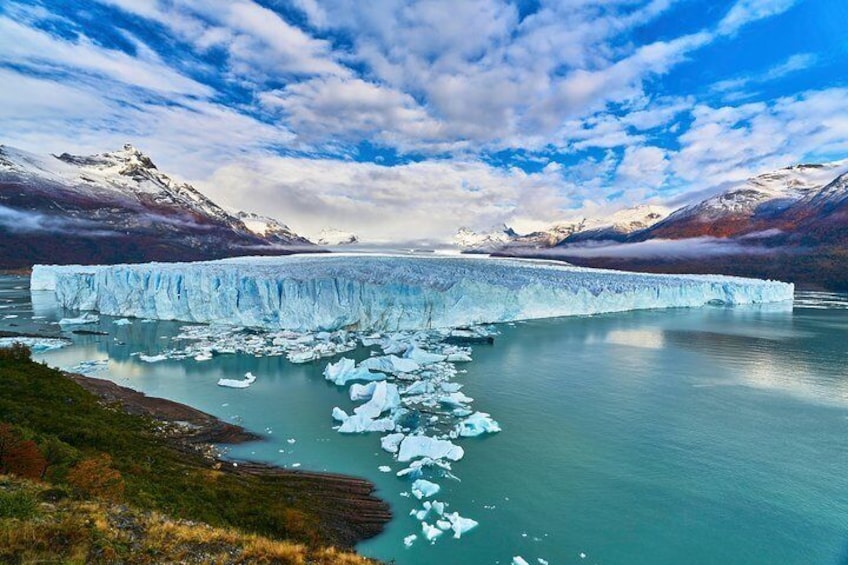 A glacier calving into a turquoise lake surrounded by mountains. 1