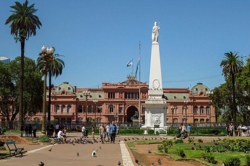 A large building with a statue, palm trees, and a park with people and pigeons. 5