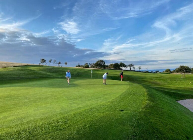 A golf course with players, a flag, and a clear sky. 4