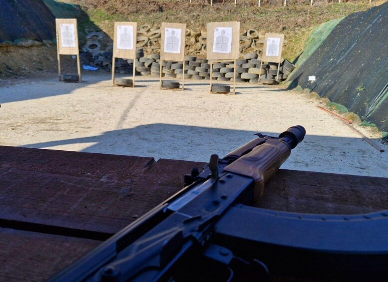 A rifle with a scope, wooden stands with target sheets, and a backdrop of tire stacks. 3