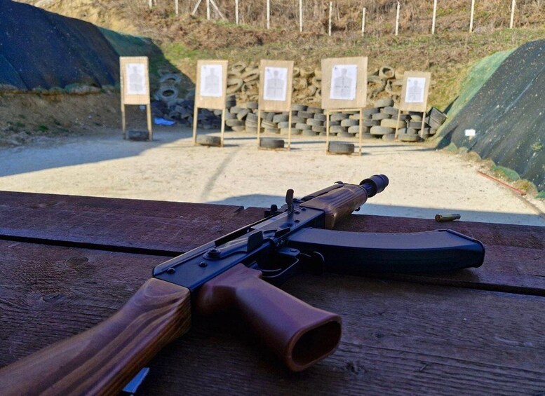 A rifle on a wooden table with a shooting range in the background. 1