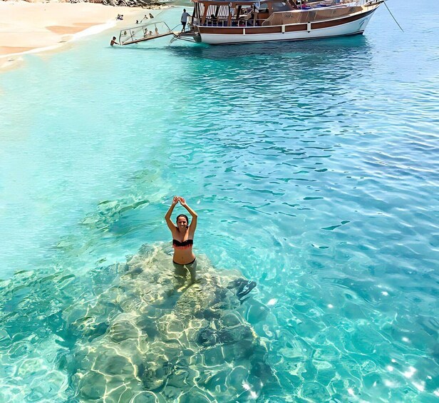 A person in a bikini performing a yoga pose in clear turquoise water with a boat in the background. 4