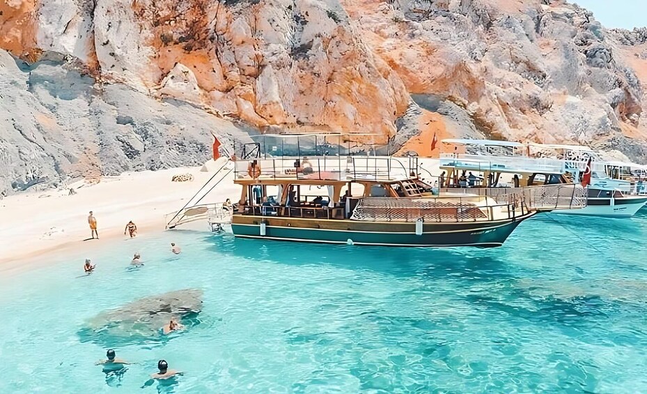 A boat docked at a beach with clear turquoise water and rocky cliffs in the background. 5