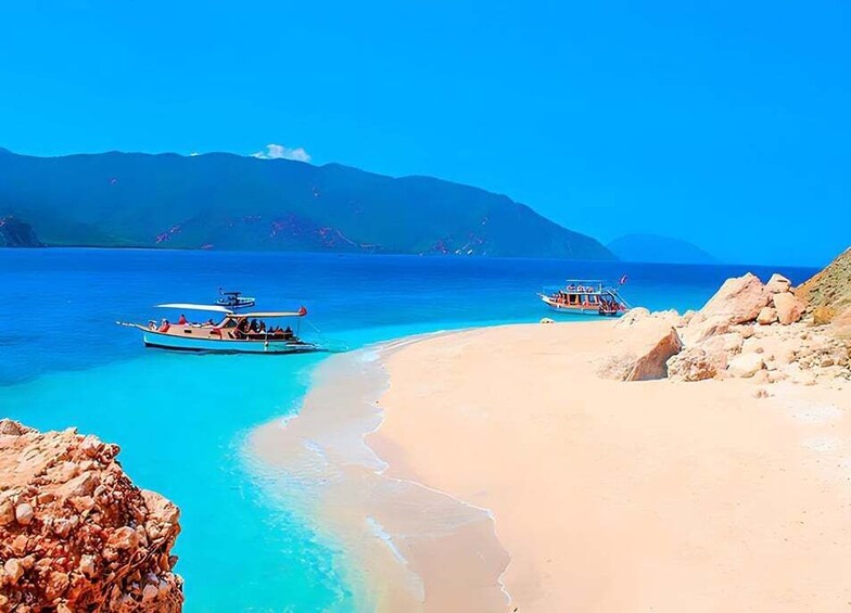 A beach with clear turquoise water, boats, and rocky outcrops. 1