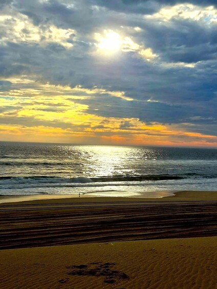A beach with waves, a person walking, and a sunset. 1