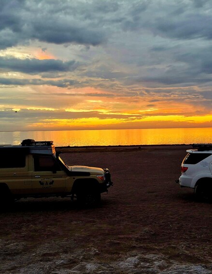 A sunset over a body of water with two vehicles parked on a dirt area. 2