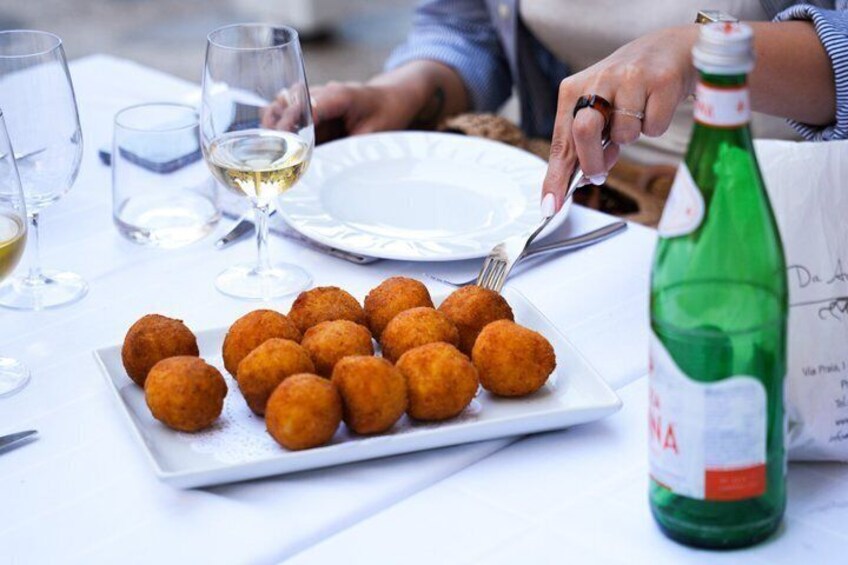 A plate of golden-brown croquettes on a white plate, a bottle of green soda, and a glass of white wine on a table. 5