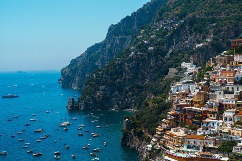 A coastal town with colorful buildings, a steep cliff, and numerous boats on the water. 3