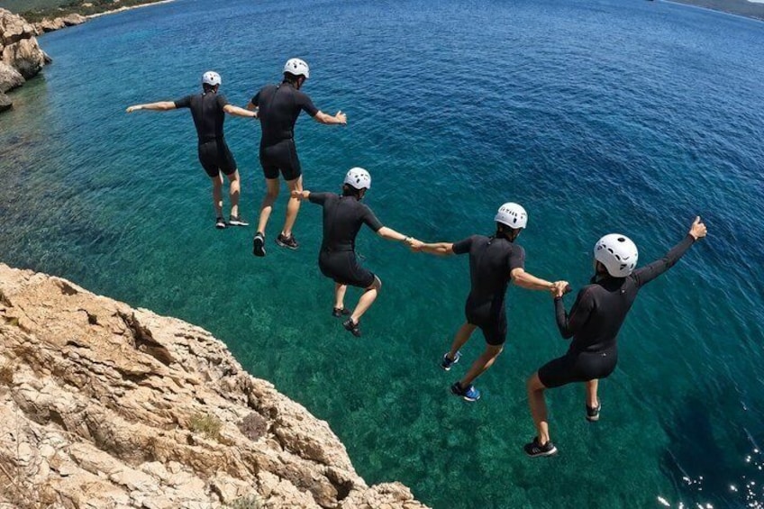 Four people jumping off a cliff into clear blue water. 1
