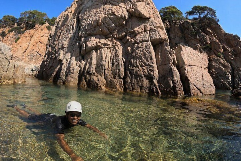 A person swimming in clear water with a rocky cliff in the background. 2