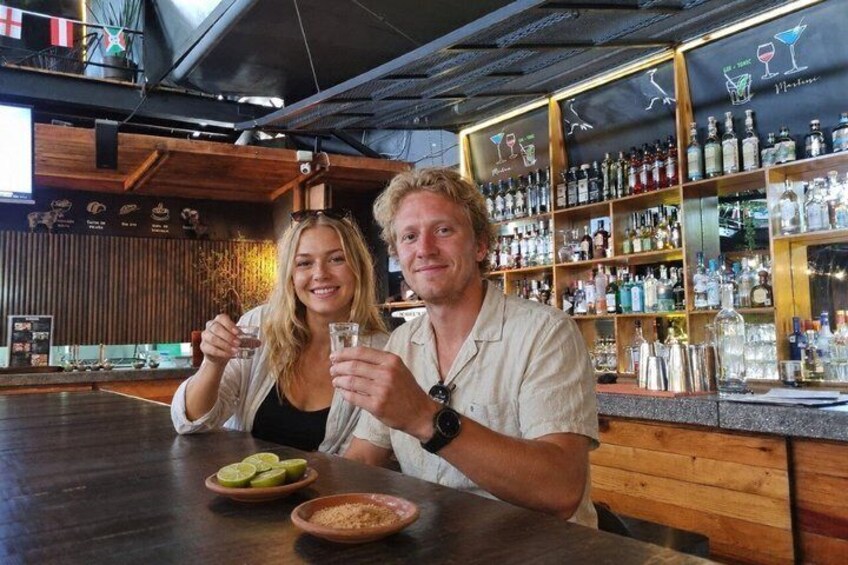 Two people sitting at a bar with a wooden interior and shelves of bottles. 5