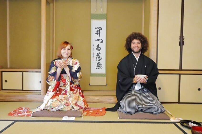 Two people in traditional Japanese attire sitting on tatami mats in a room with sliding doors and a hanging scroll. 5