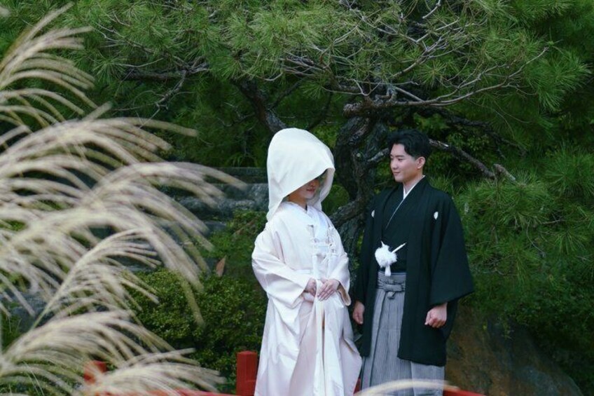 A person in traditional attire standing in a garden with a tree and foliage in the background. 3