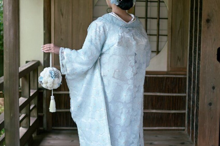 A person in a light blue kimono holding a decorative item, standing in a wooden structure with a wooden railing. 4