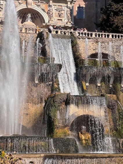 A multi-tiered water fountain with statues, set against a classical building facade. 3