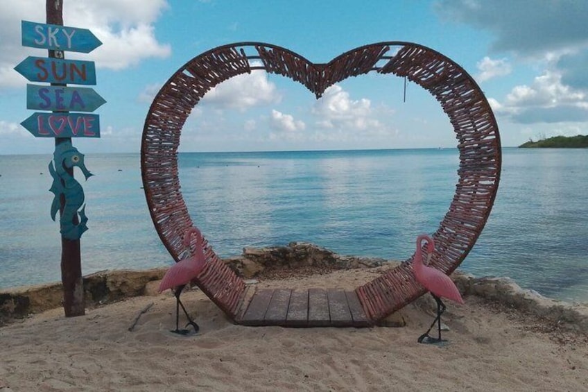 A heart-shaped structure on a beach with flamingos and a signpost with 'SKY,' 'SUN,' 'SEA,' and 'LOVE' written on it. 3