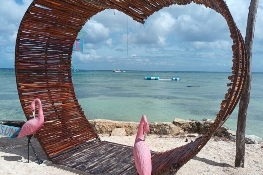 A beach scene with a wooden archway, two pink flamingos, and a clear blue sea. 1