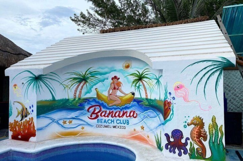 A colorful mural with a woman in a bikini on a banana boat, palm trees, and sea creatures, labeled 'Banana Beach Club.' 2