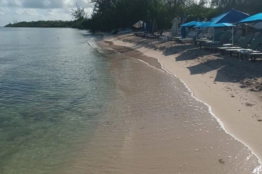 A beach with clear water, a sandy shore, and blue umbrellas. 5