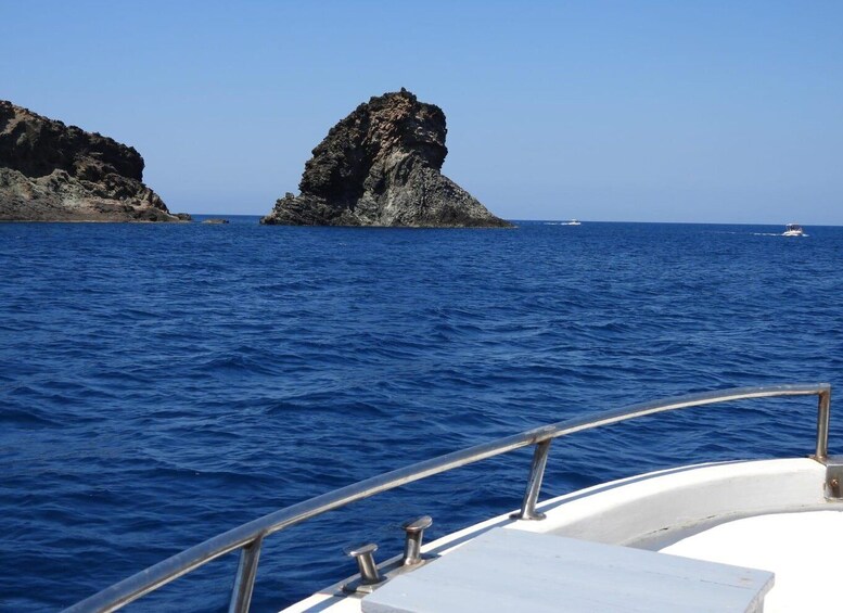 A boat on a clear blue sea with a rocky outcrop in the distance. 2