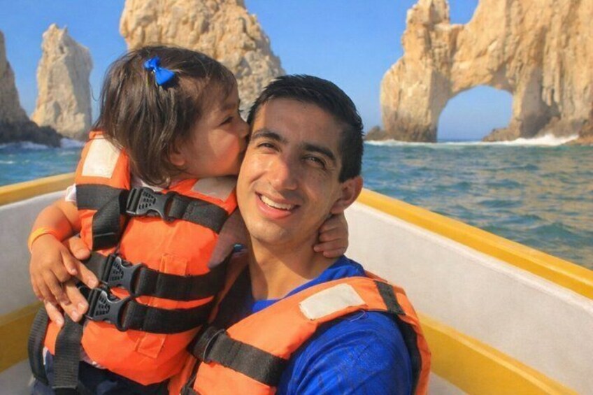A person in a boat wearing a life jacket, with a rocky coastline and a distinctive rock formation in the background. 2