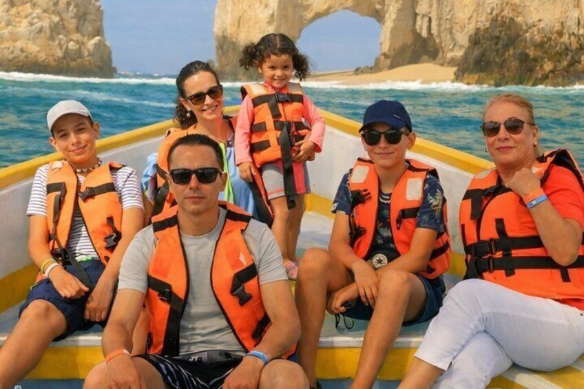 A group of people on a boat with life jackets, a rocky coastline, and a sea arch in the background. 5