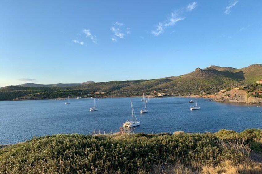 A coastal bay with sailboats anchored, surrounded by hills and sparse vegetation. 5