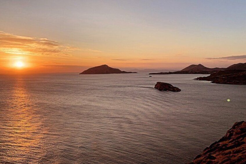 A sunset over calm waters with distant islands and rocky outcrops. 2