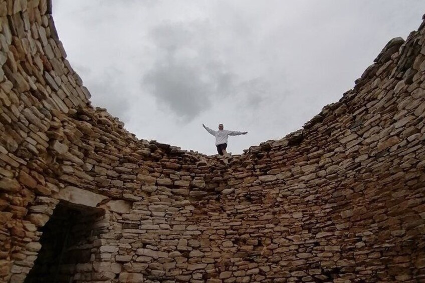 A person standing in a stone structure with a wide opening at the top. 3