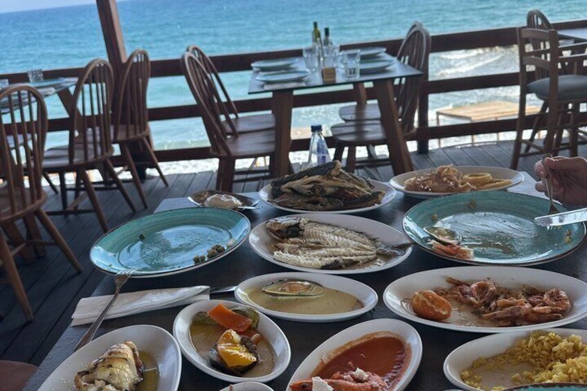 A table with various seafood dishes, wooden chairs, and a view of the ocean. 4