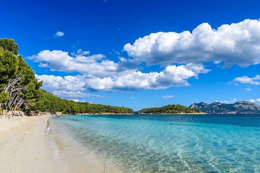 A beach with clear turquoise water, sandy shore, and green hills in the background. 1
