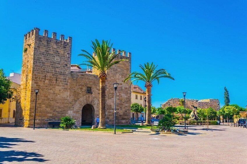Un edificio histórico de piedra con una torre, palmeras y un cielo azul despejado. 4
