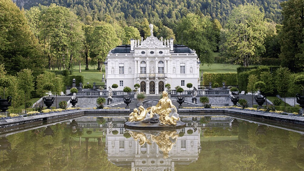 A grand white building with a large fountain in front, surrounded by lush greenery. 1