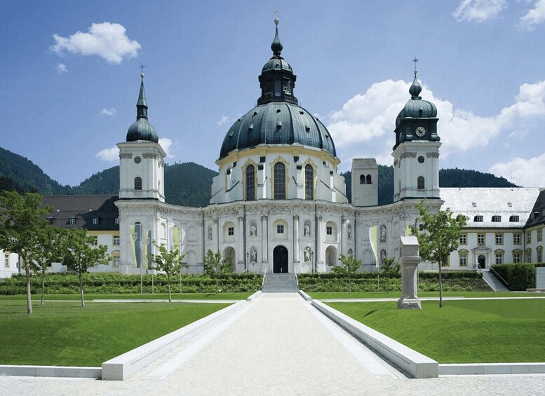 A grand historical building with two domes and a central dome, surrounded by a well-maintained lawn and a clear sky. 3