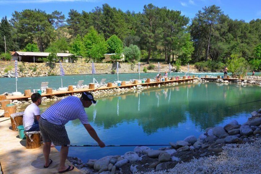 A man fishing at a calm lake with a dock, surrounded by trees and rocks. 3