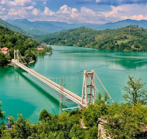 A suspension bridge over a turquoise river, surrounded by lush green hills and a clear sky. 1