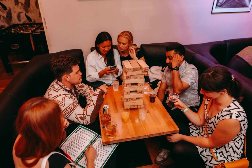 A group of people playing Jenga at a wooden table with drinks. 3