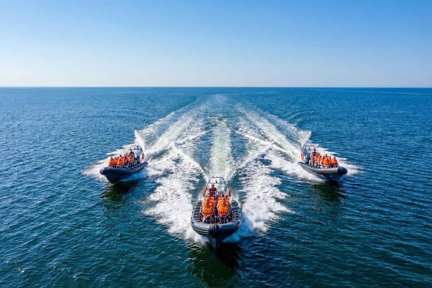 Three boats with people wearing life jackets in formation on the water. 4