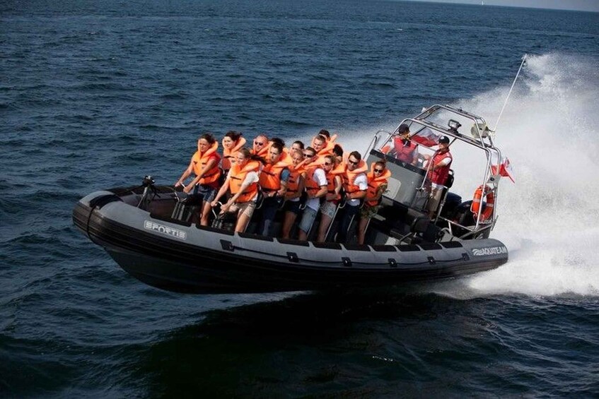 A group of people on a boat with life jackets, moving through the water. 2