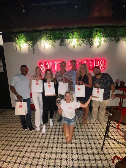 A group of people holding shopping bags in front of a neon sign that reads 'SALTSSSTEDS.' 1