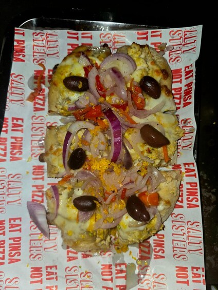 A pizza with toppings like onions, olives, and bell peppers on a paper with text. 3