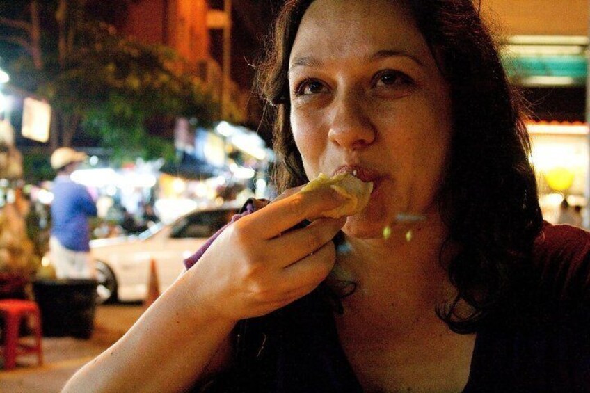 A person eating a sandwich outdoors at night. 1