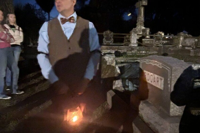 A person in a vest and bow tie standing near a tombstone labeled 'ROGART' at night. 3